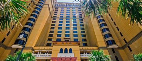 A tall, multi-story hotel with a symmetrical facade, featuring balconies and a central entrance with an archway.