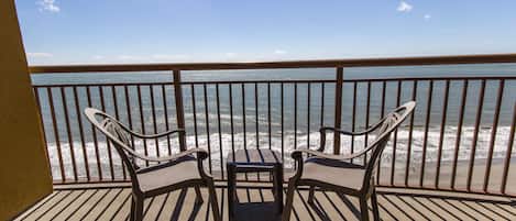 A balcony with two chairs and a small table, overlooking the ocean.