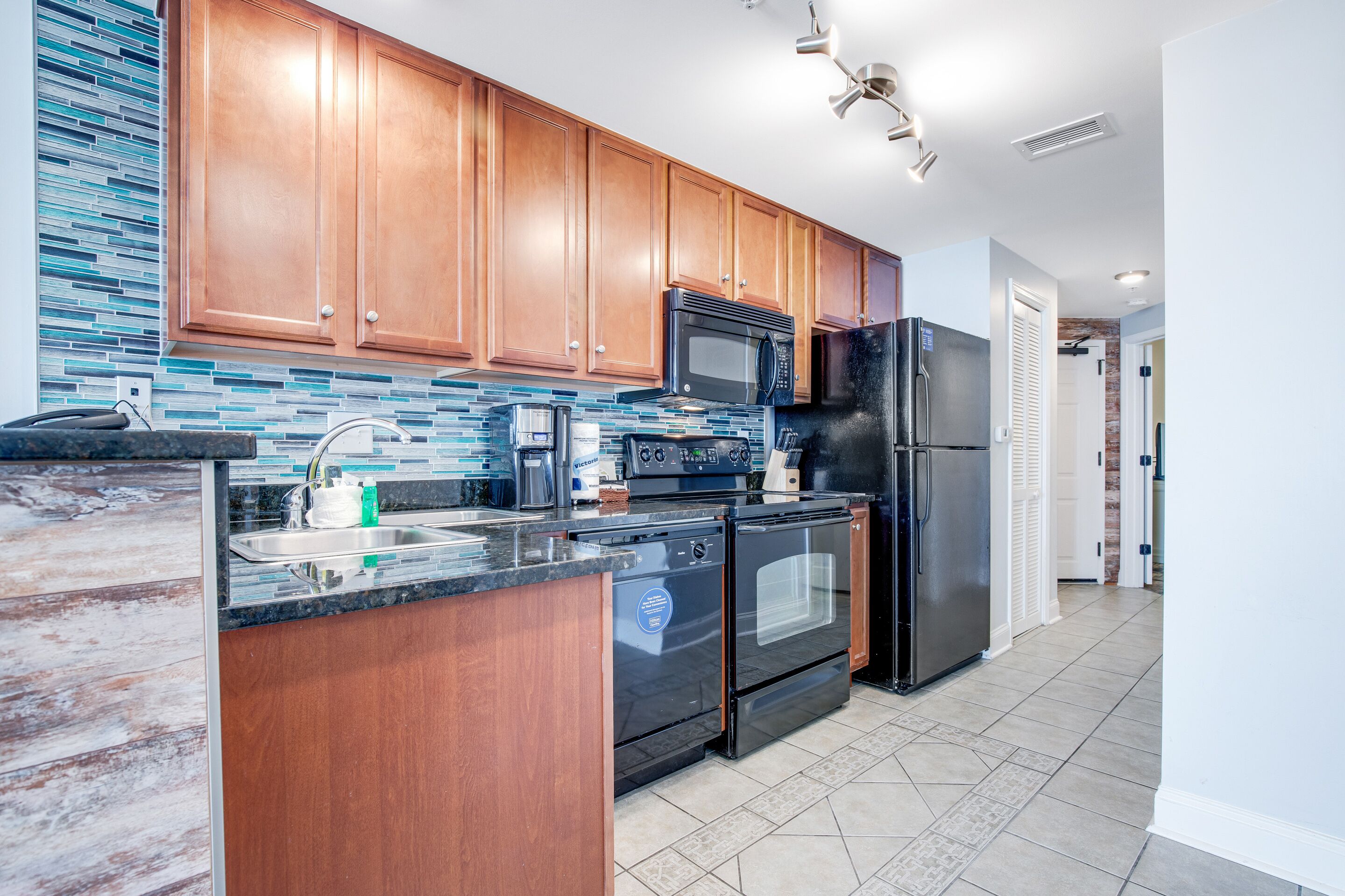 A modern kitchen with wooden cabinets, a stainless steel refrigerator, a microwave, an oven, and a sink.