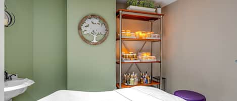 A room with a bed, a shelf with toiletries, a wall-mounted mirror, and a small plant.