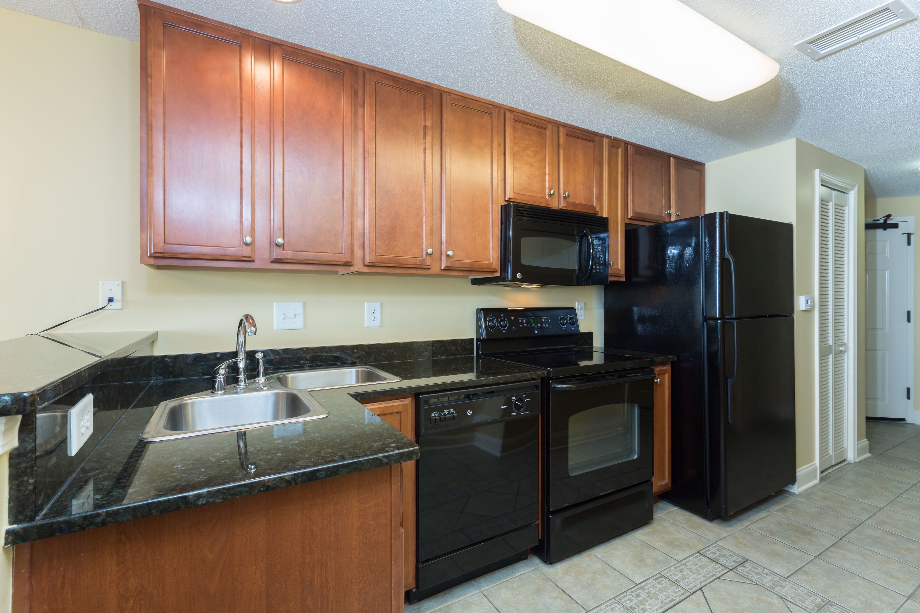 A kitchen with wooden cabinets, a black refrigerator, a microwave, a dishwasher, and a granite countertop.
