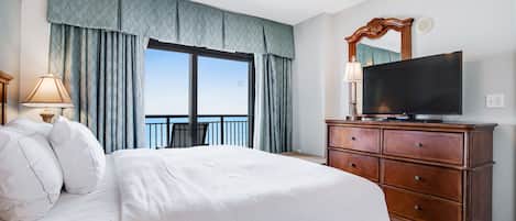Een hotelkamer met een groot bed, een houten dressoir, een televisie en een balkon met gordijnen.