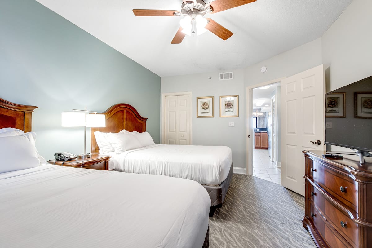 Une chambre d’hôtel avec deux lits, une commode en bois, un ventilateur de plafond et des tableaux encadrés accrochés au mur.