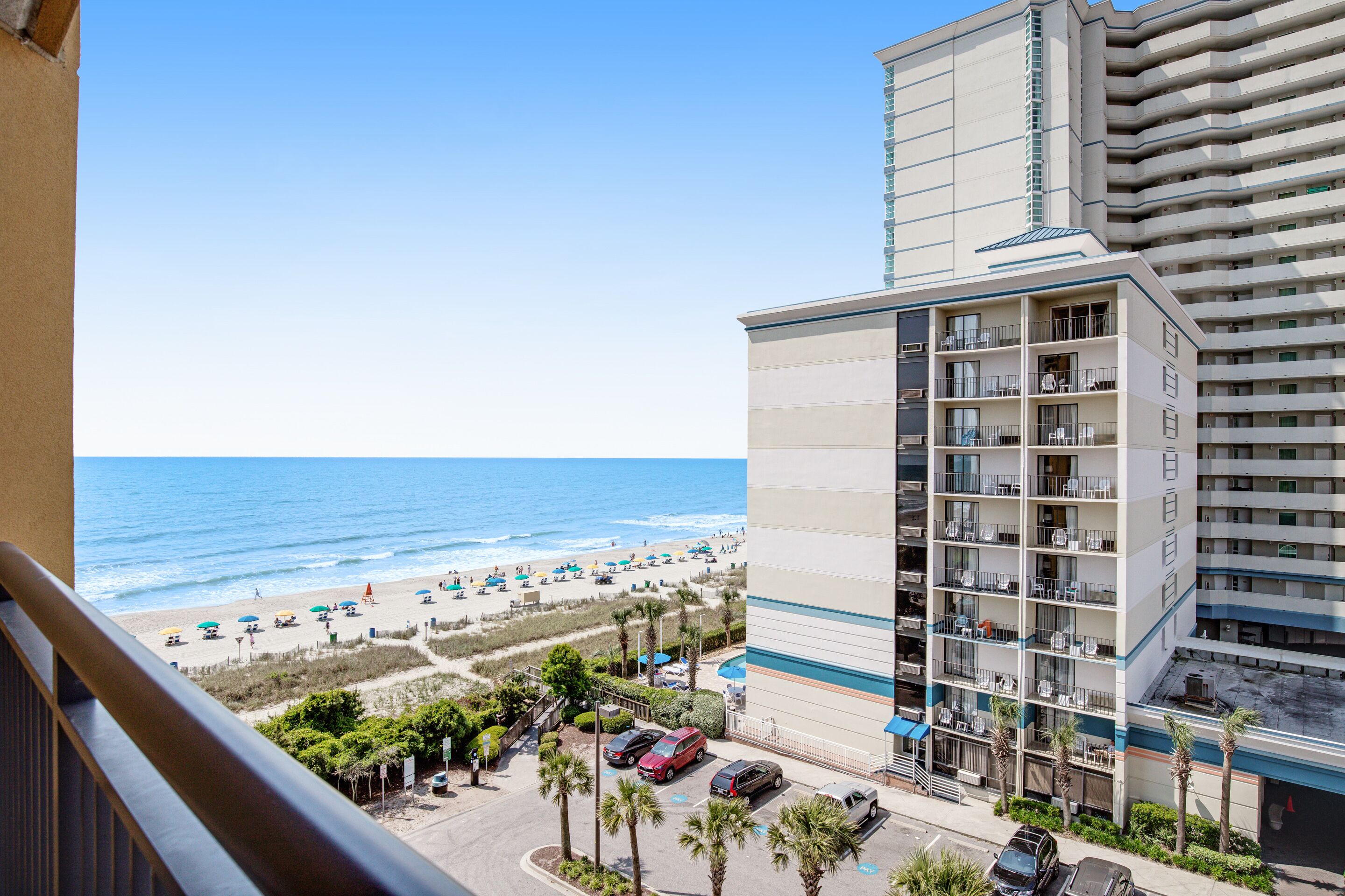 Un hôtel avec vue sur la plage, doté de nombreux balcons et d’un parking pouvant accueillir plusieurs voitures.
