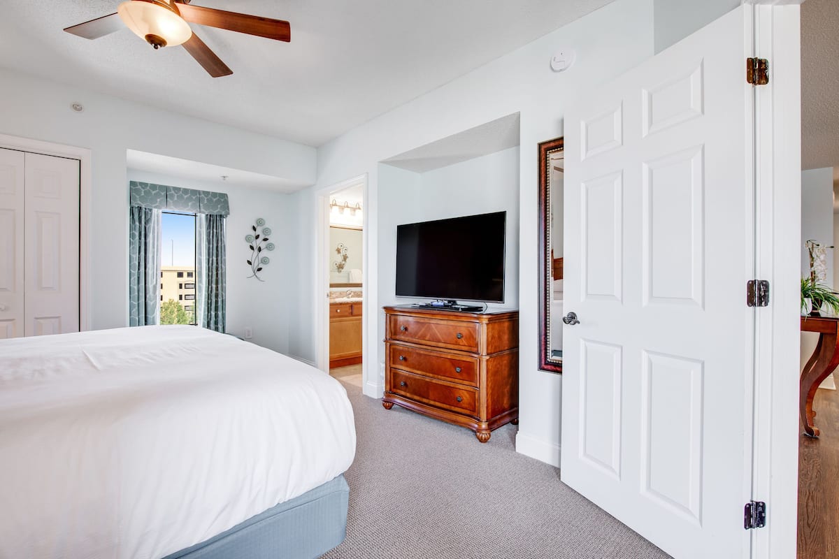 Une chambre à coucher comprenant un lit, une commode, un téléviseur et une porte donnant sur une autre pièce.