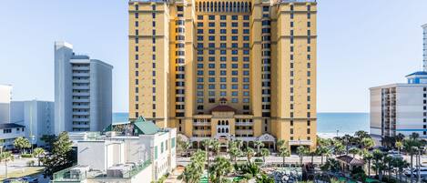 A high-rise hotel with multiple floors, a central courtyard with palm trees, and a view of the ocean.