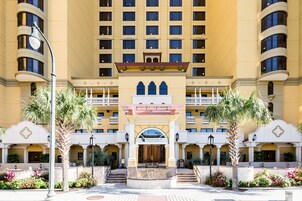 A hotel with a central entrance, multiple balconies, and a courtyard with palm trees.