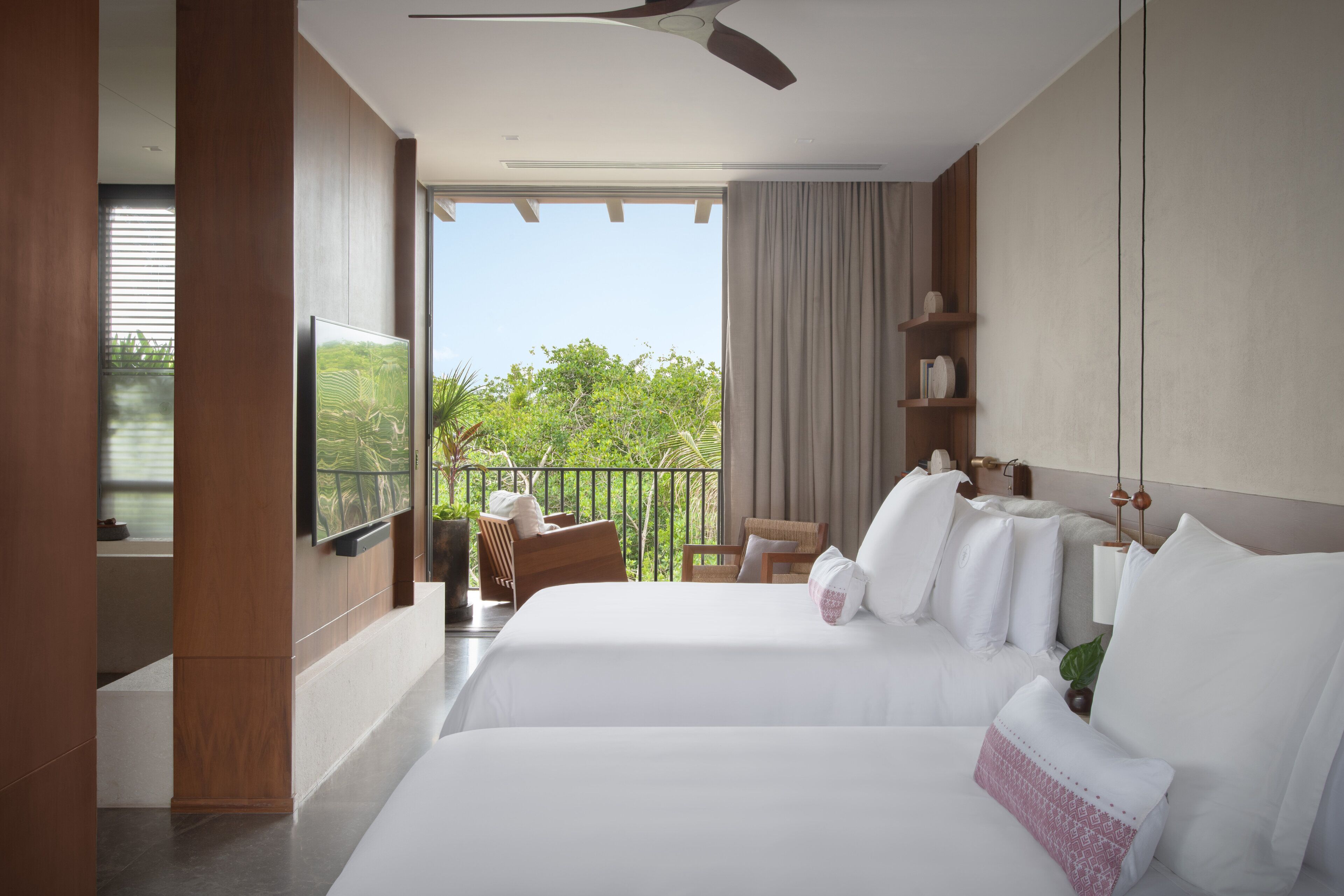 Une chambre d’hôtel avec un balcon, un lit avec du linge de lit blanc, un ventilateur de plafond et un téléviseur fixé au mur.