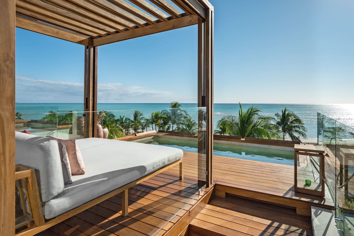 A balcony with a bed, glass walls, and a view of the ocean.