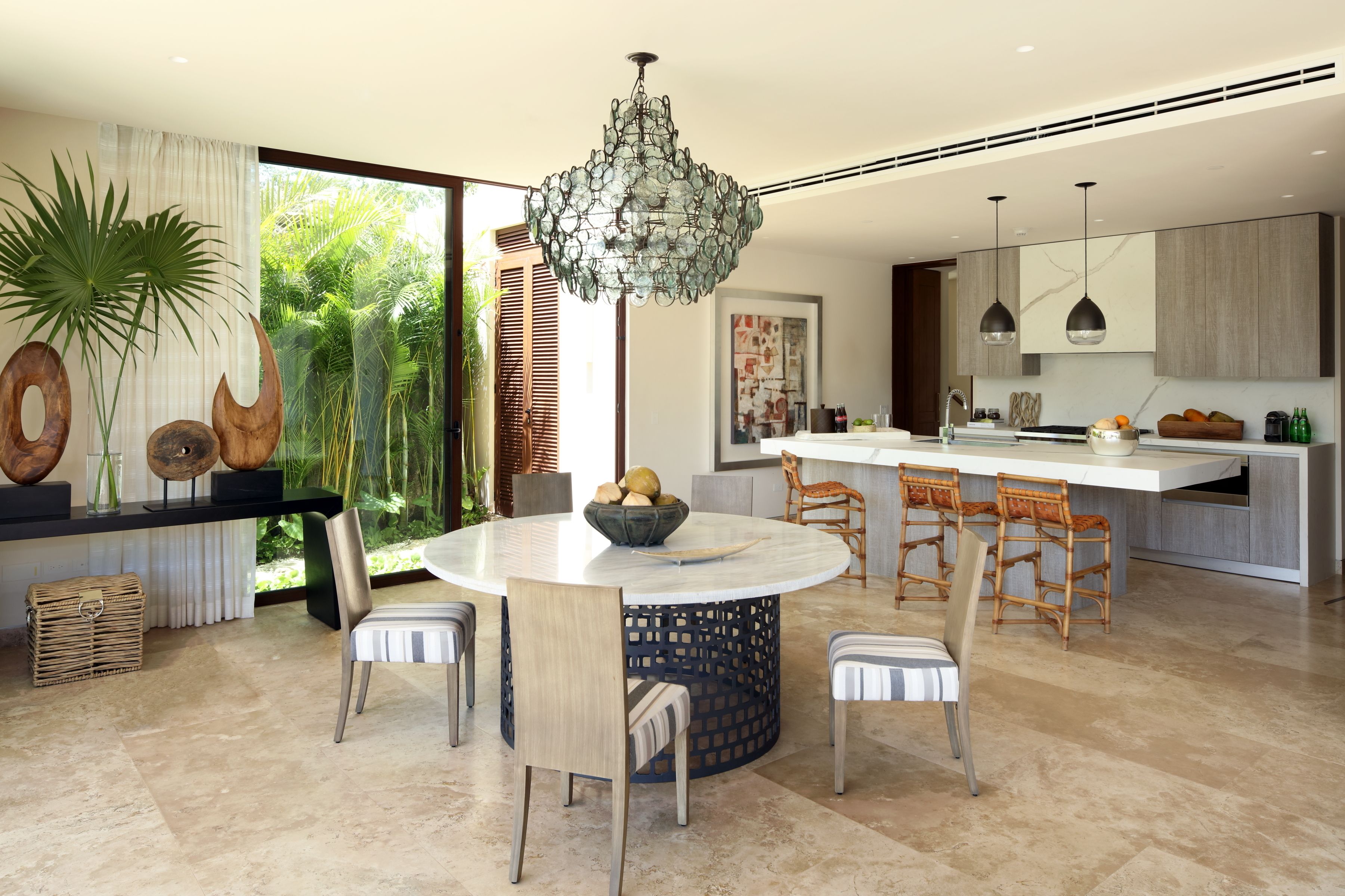 A modern kitchen with a central island, dining area with chairs, and a chandelier.