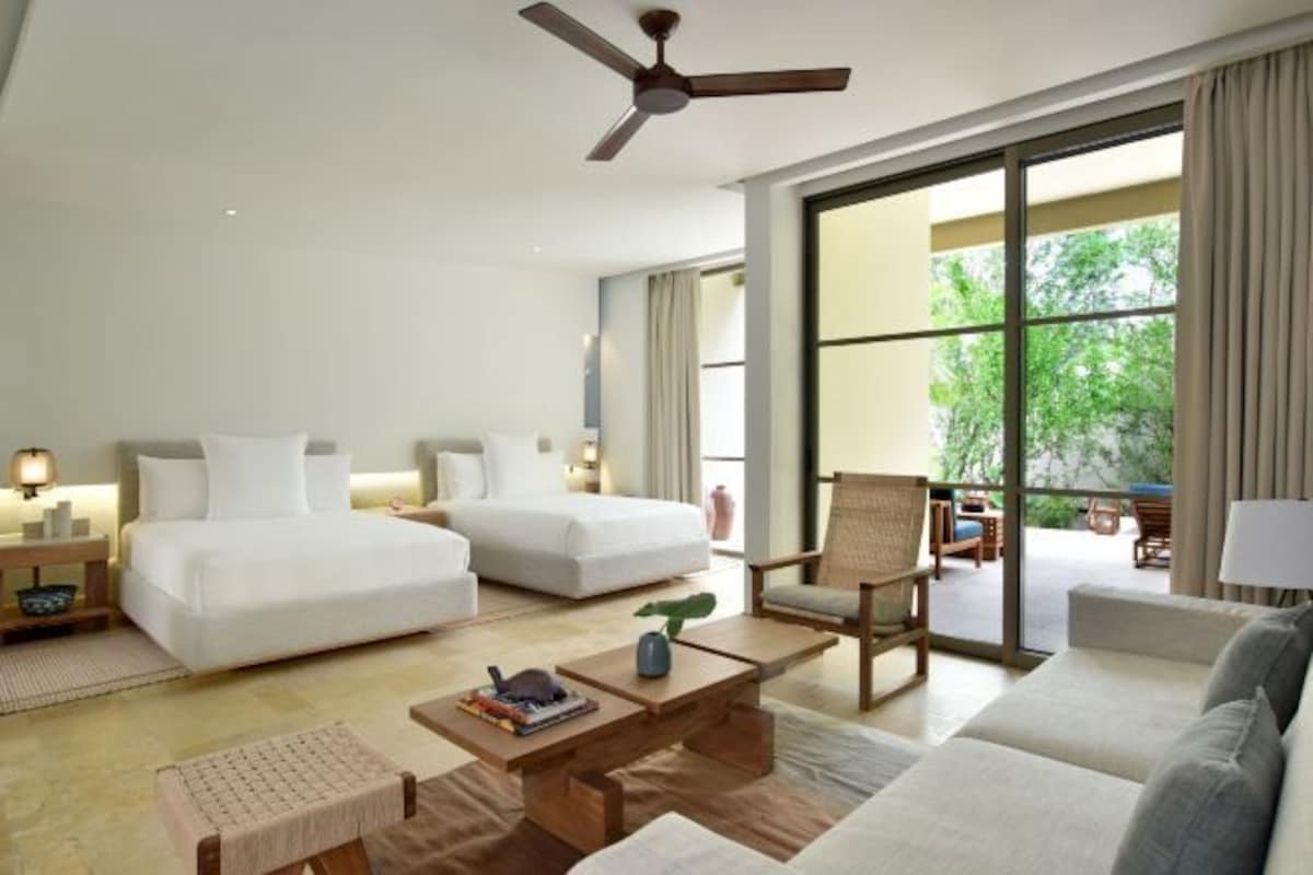 Habitación de hotel con dos camas, un sofá, una mesa de centro, una silla y un ventilador de techo.