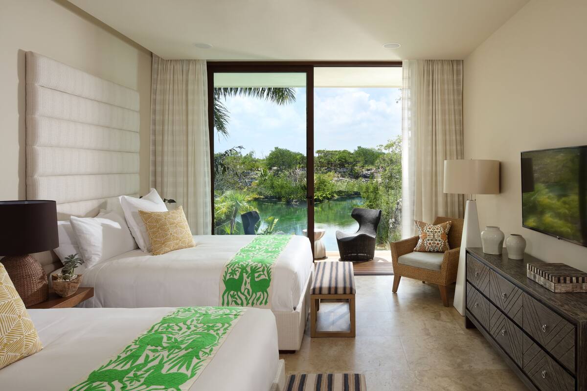 A hotel room with two beds, a sofa, a TV, and a view of a lake.