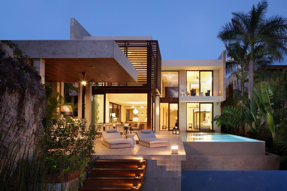 A modern house with a swimming pool, outdoor seating, and a well-lit interior.