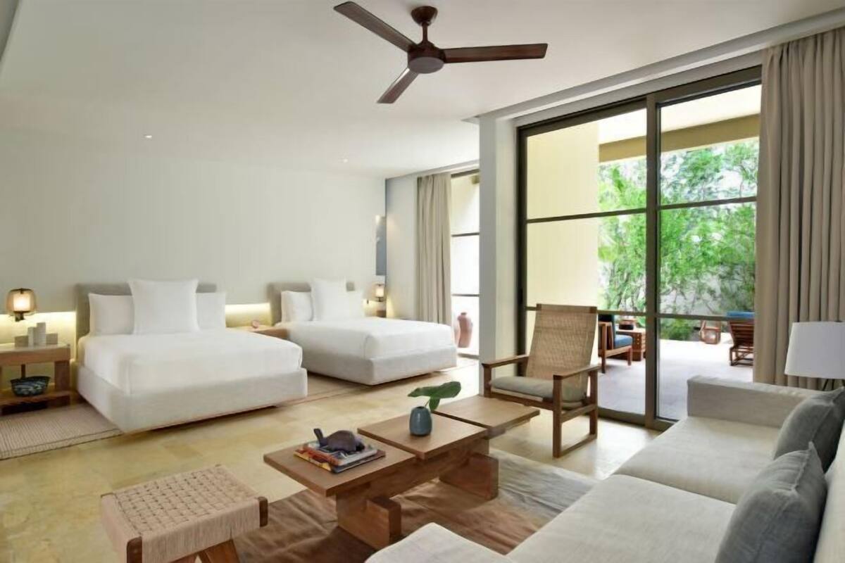 A hotel room with two beds, a sofa, a coffee table, a chair, and a ceiling fan.