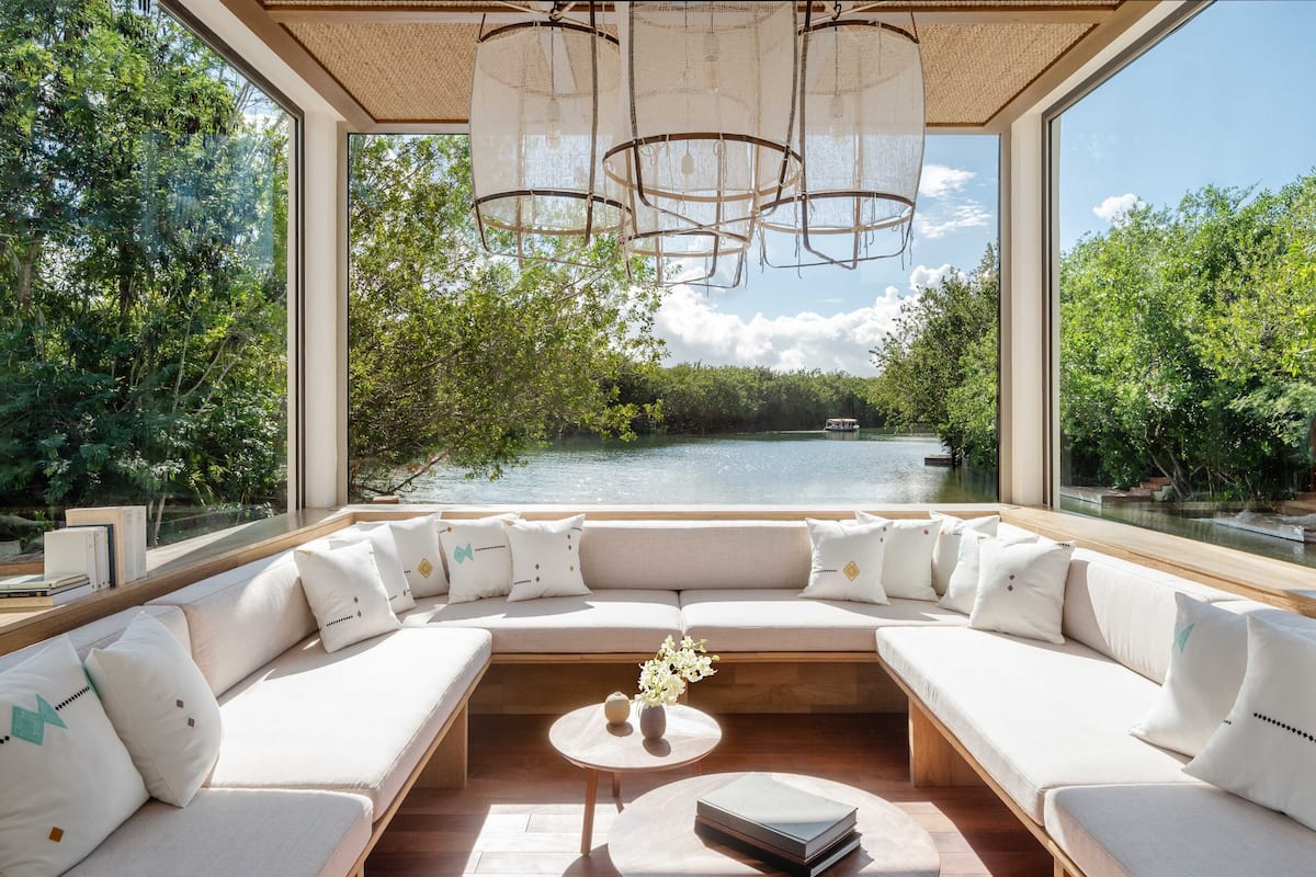 A modern, open-plan living area with a large window overlooking a body of water and lush greenery.