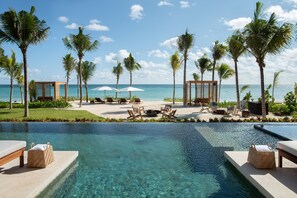 A poolside area with lounge chairs, umbrellas, and a view of the ocean. - Rosewood Mayakoba (Playa del Carmen)