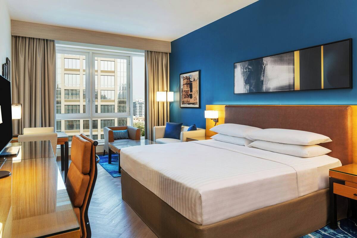 A hotel room with a large bed, a desk, a chair, a sofa, and a window with curtains.