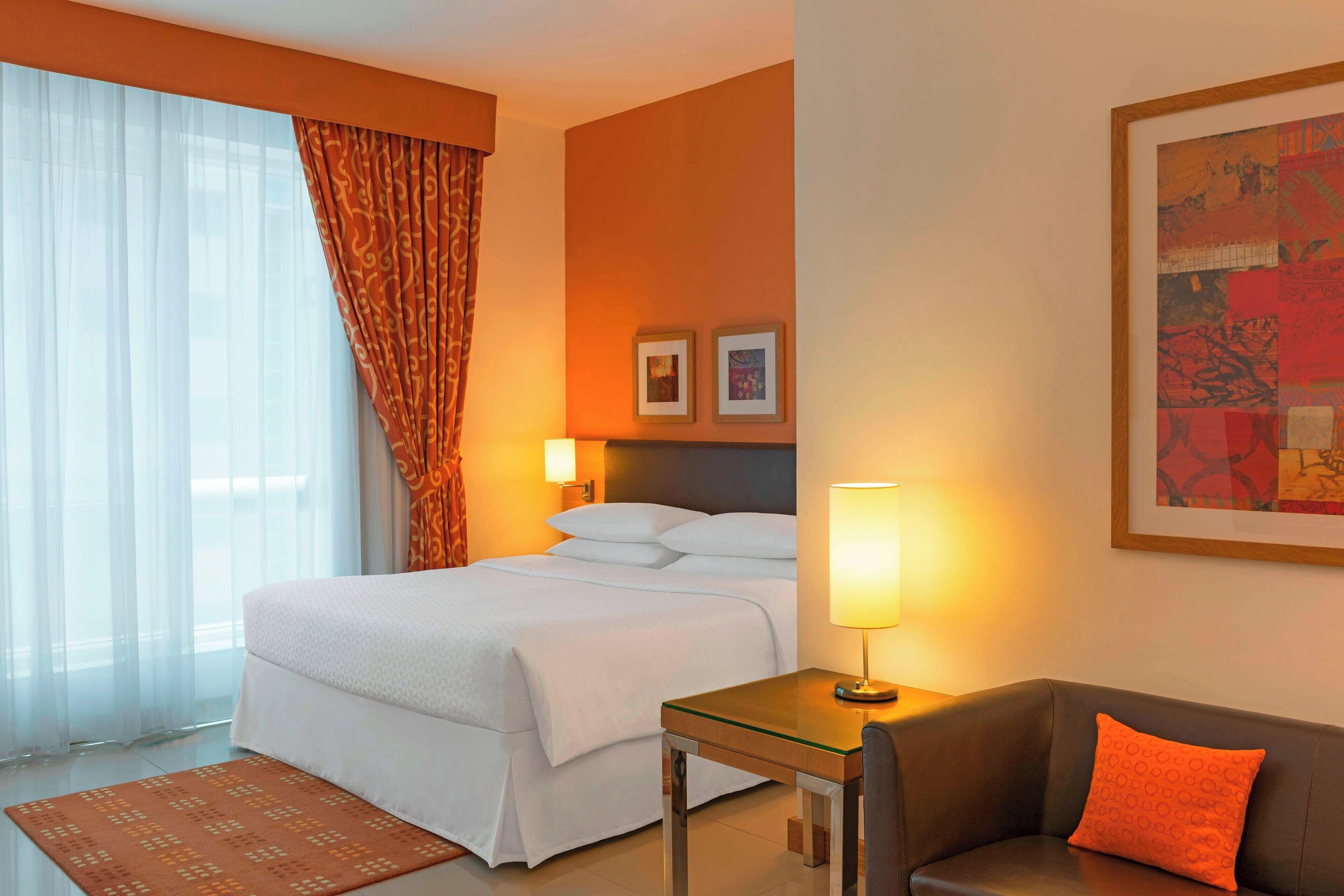 Ein Hotelzimmer mit Bett, Schreibtisch, Sofa, einem Fenster mit Vorhängen und zwei gerahmten Bildern an der Wand.