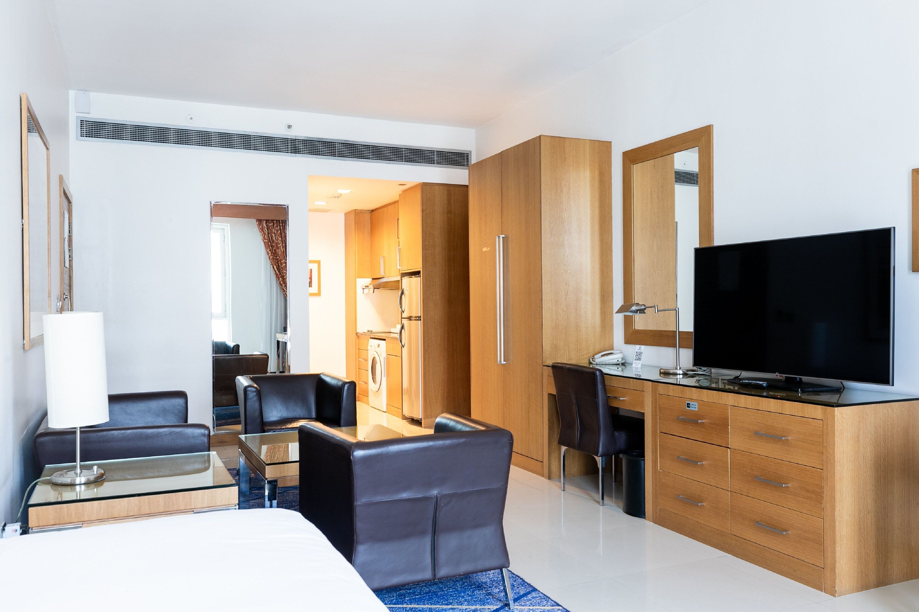 Une chambre d’hôtel comprenant un lit, un bureau avec une télévision, un coin repas avec des chaises et un coin cuisine.