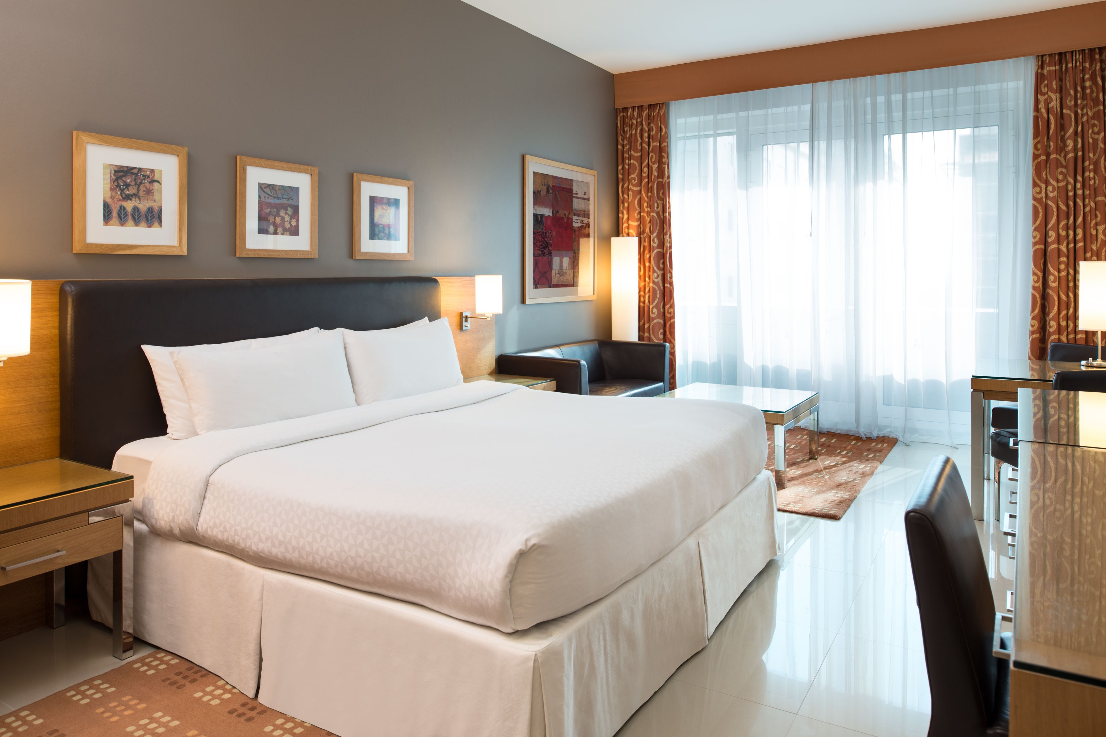 A hotel room with a large bed, a desk, a chair, and a window with curtains.