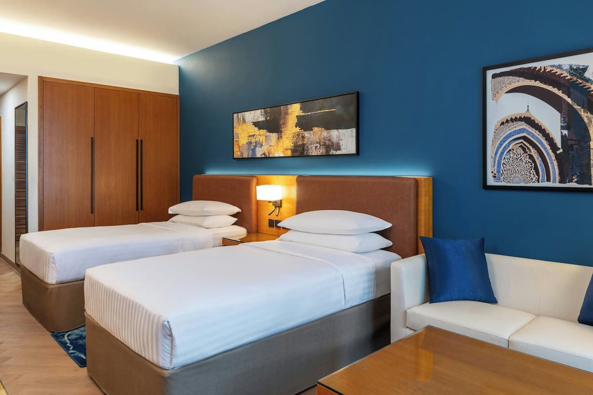 A hotel room with two beds, a sofa, a wardrobe, and artwork on the walls.