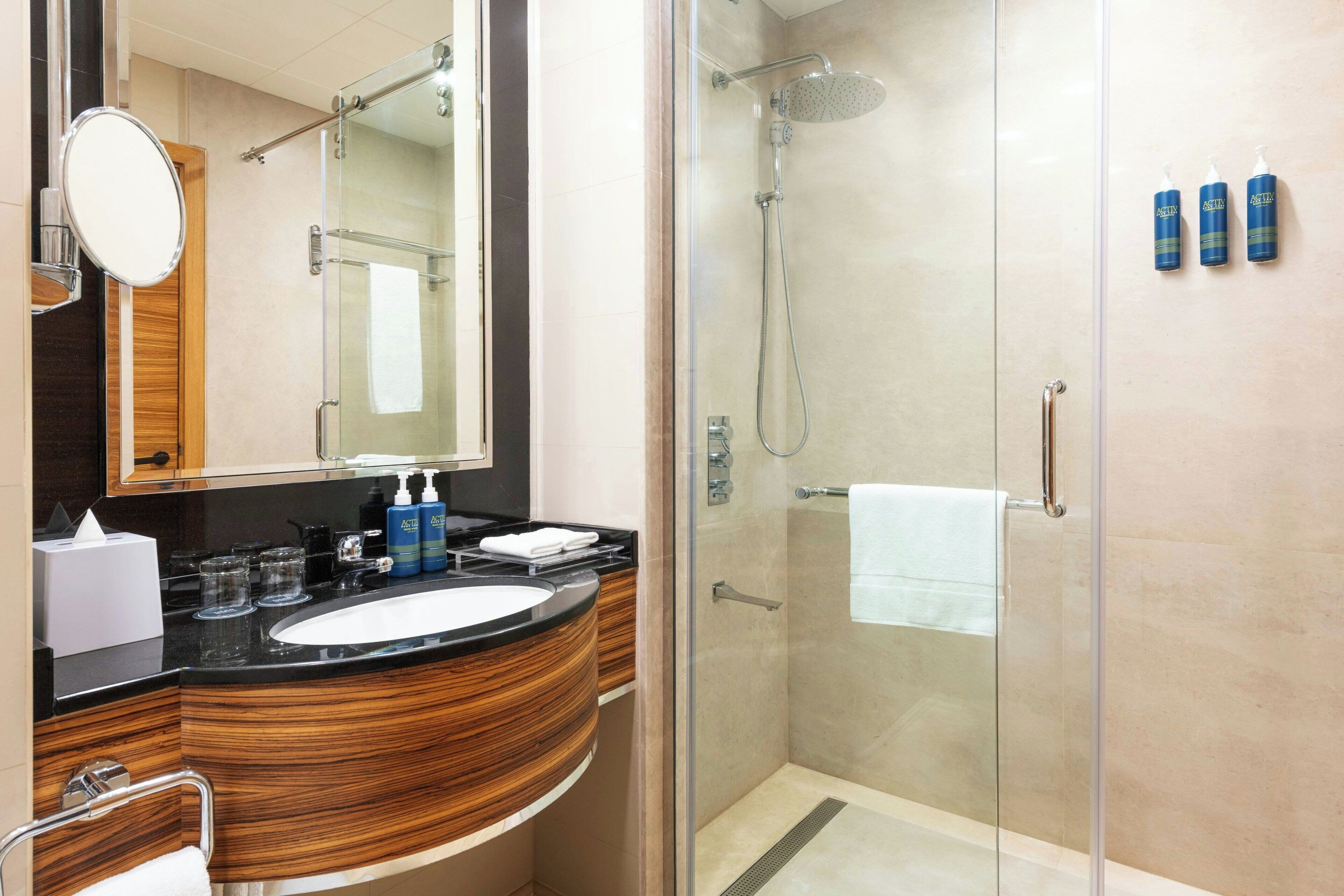 A modern bathroom with a glass-enclosed shower, a wooden vanity with a sink, and toiletries on the counter.
