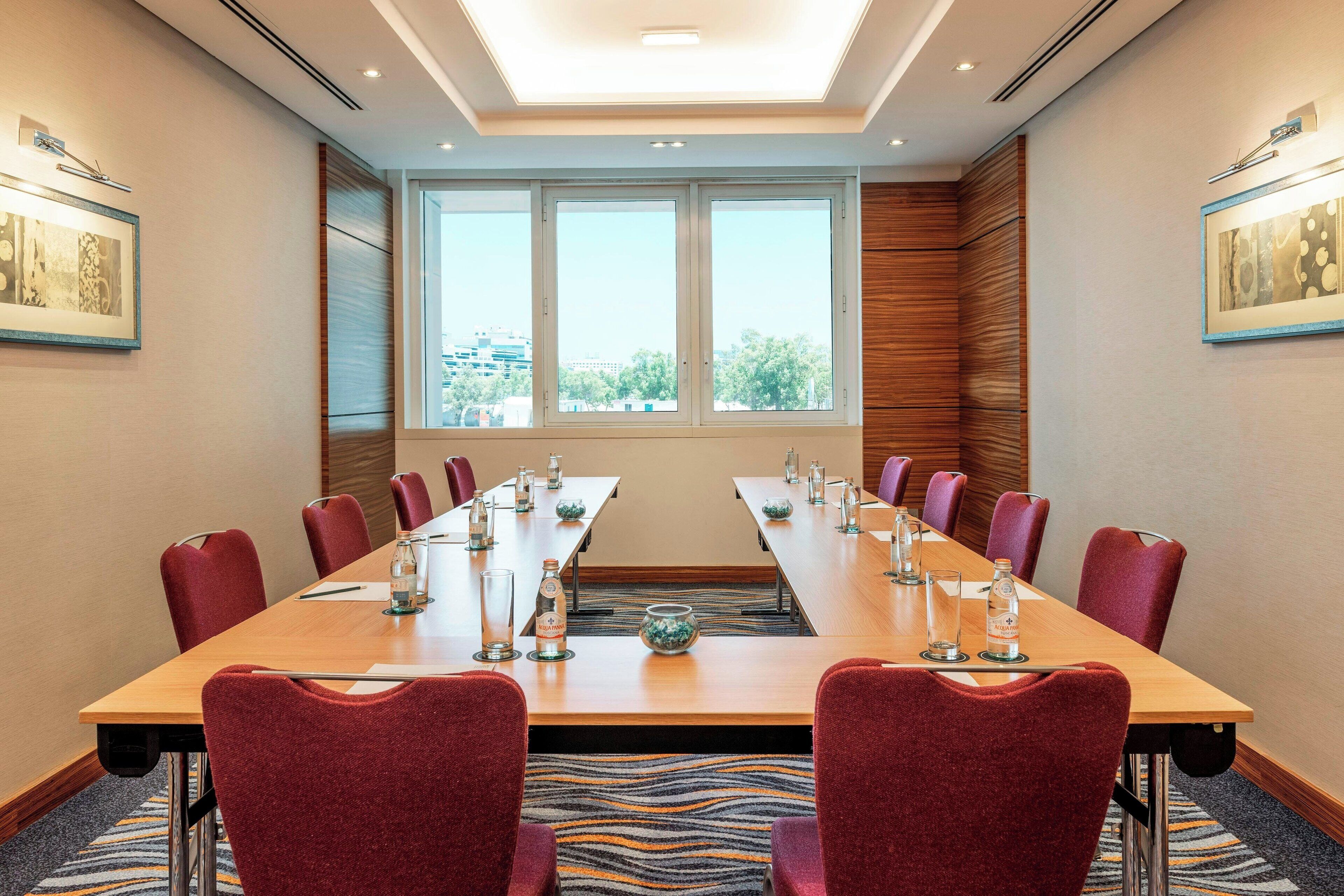 A conference room with a long table, red chairs, and a view through large windows.