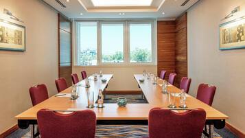 A conference room with a long table, red chairs, and a view through large windows.
