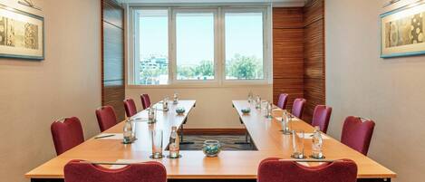 A conference room with a long table, red chairs, and a view through large windows.