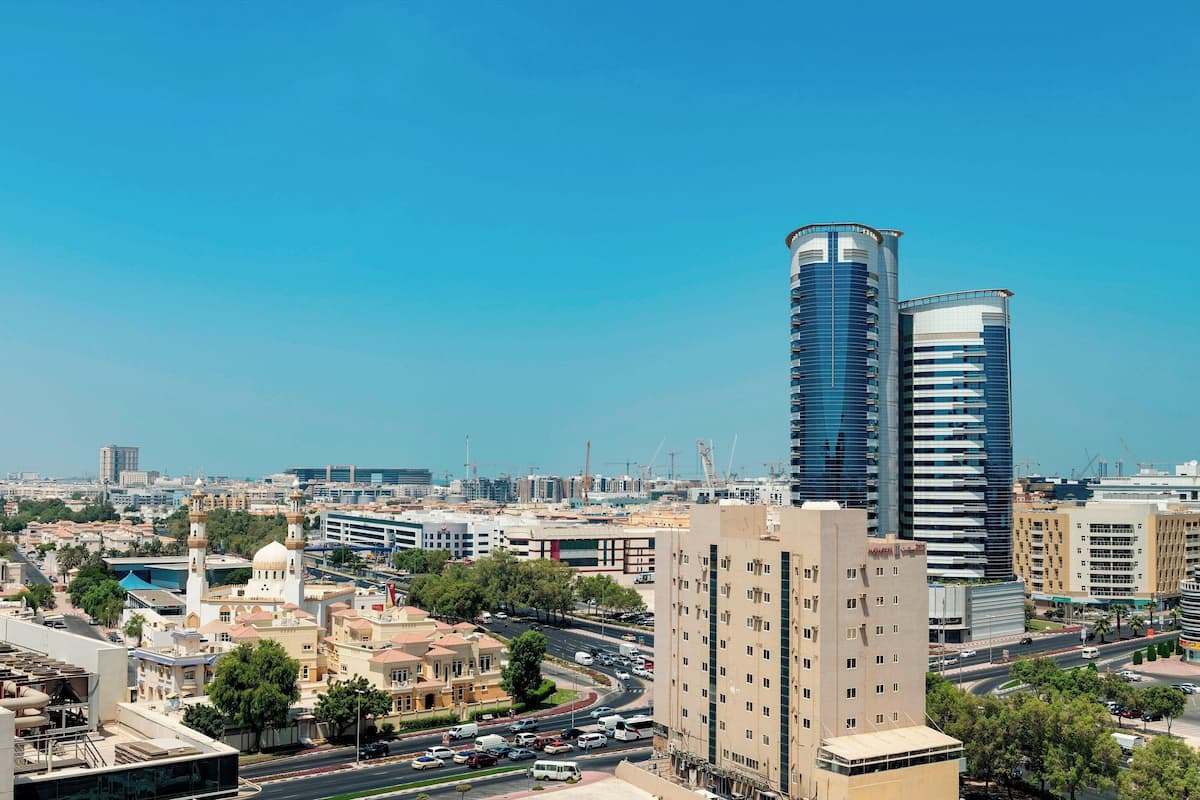 A cityscape with modern high-rise buildings, a mosque with a dome and minarets, and a busy road with vehicles.