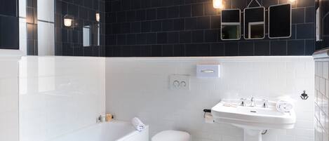 Um banheiro moderno com parede revestida de azulejos pretos, pia branca e banheira.