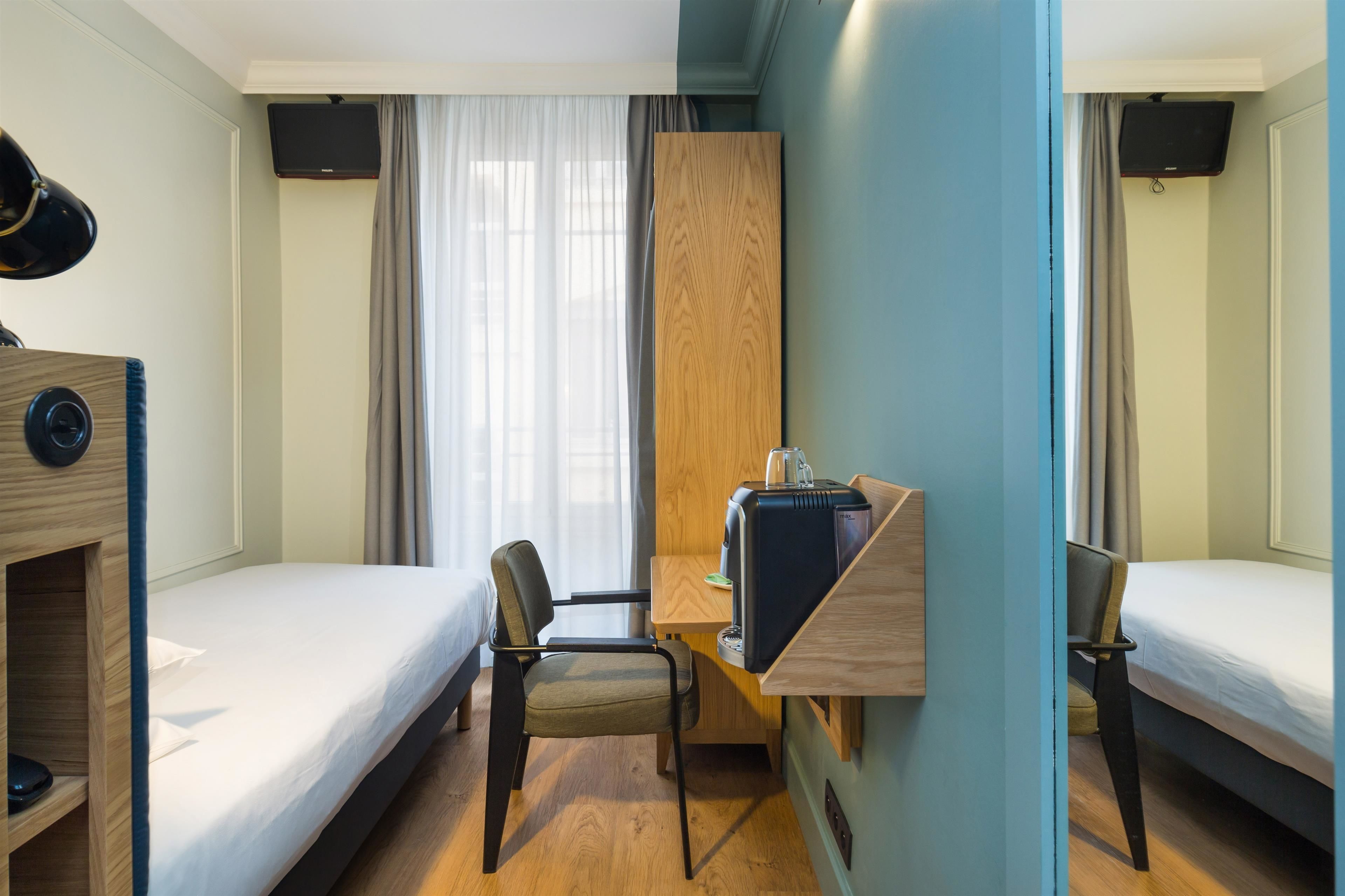 A hotel room with two single beds, a desk with a chair, a television mounted on the wall, and a window with curtains.