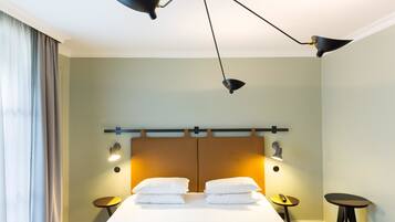 Una habitación de hotel con una cama grande, dos mesitas de noche, una lámpara de techo moderna y una ventana con cortinas.