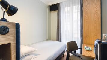 Une chambre d’hôtel avec un lit simple, un bureau avec une chaise, une machine à café et un téléviseur fixé au mur.