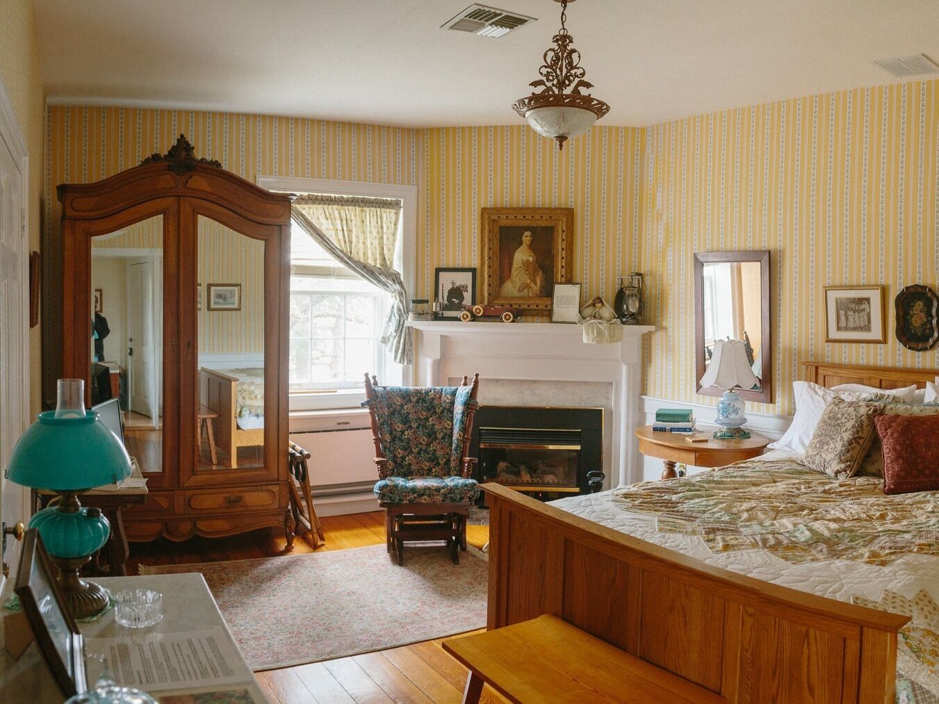 Une chambre traditionnelle avec un grand lit, une cheminée, un miroir et une commode en bois.