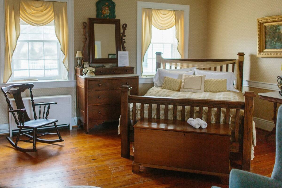 A traditional bedroom with a wooden bed, a rocking chair, a dresser, and a mirror.