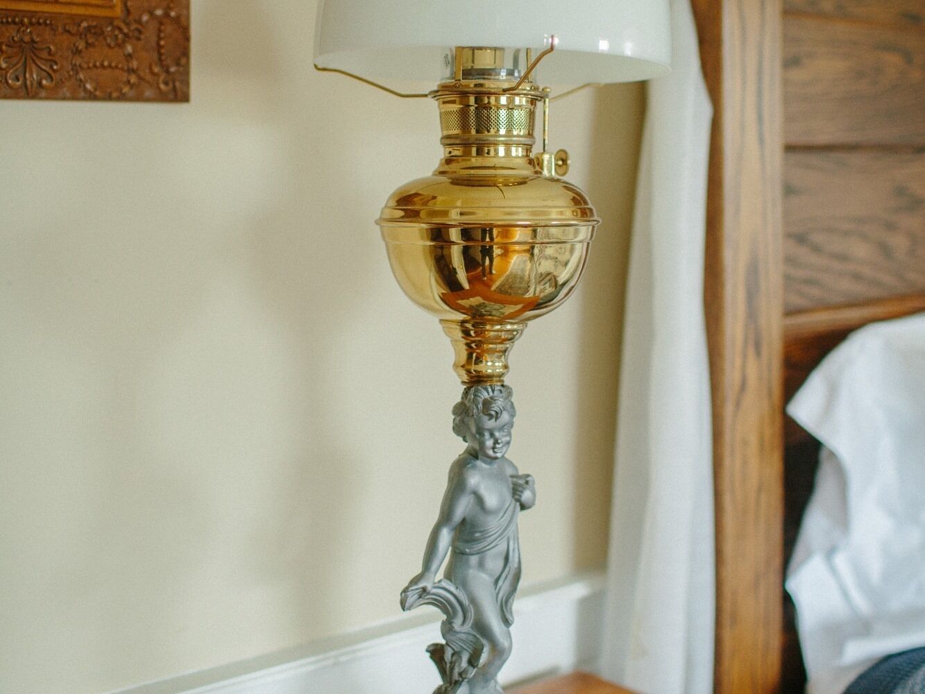 En lampa i mässing med en vit lampskärm och en dekorativ figur på foten.