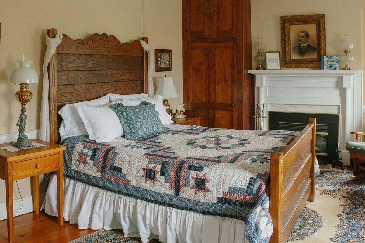 A traditional bedroom with a wooden bed, a white fireplace, and a classic decor style.