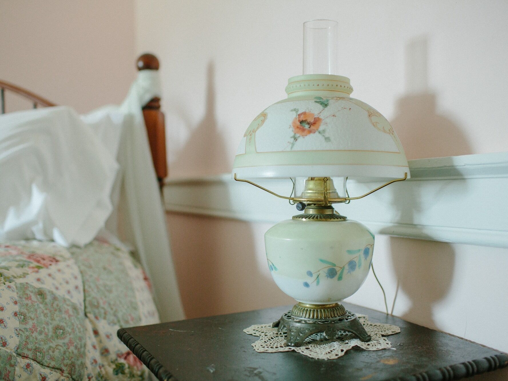 A vintage table lamp with floral patterns on a bedside table in a bedroom.