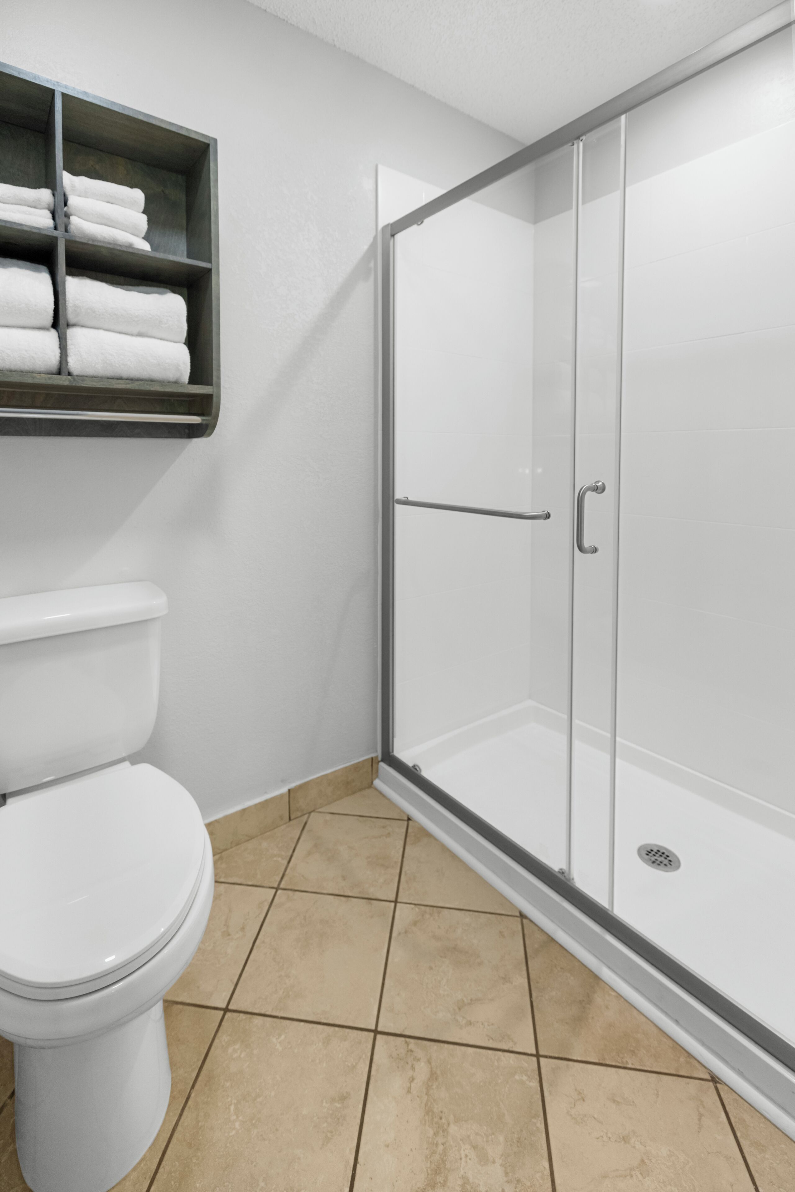 Une salle de bain comprenant des toilettes, une douche à parois de verre et une étagère avec des serviettes pliées.