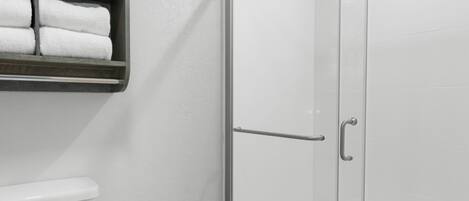 Une salle de bain comprenant des toilettes, une douche à parois de verre et une étagère avec des serviettes pliées.