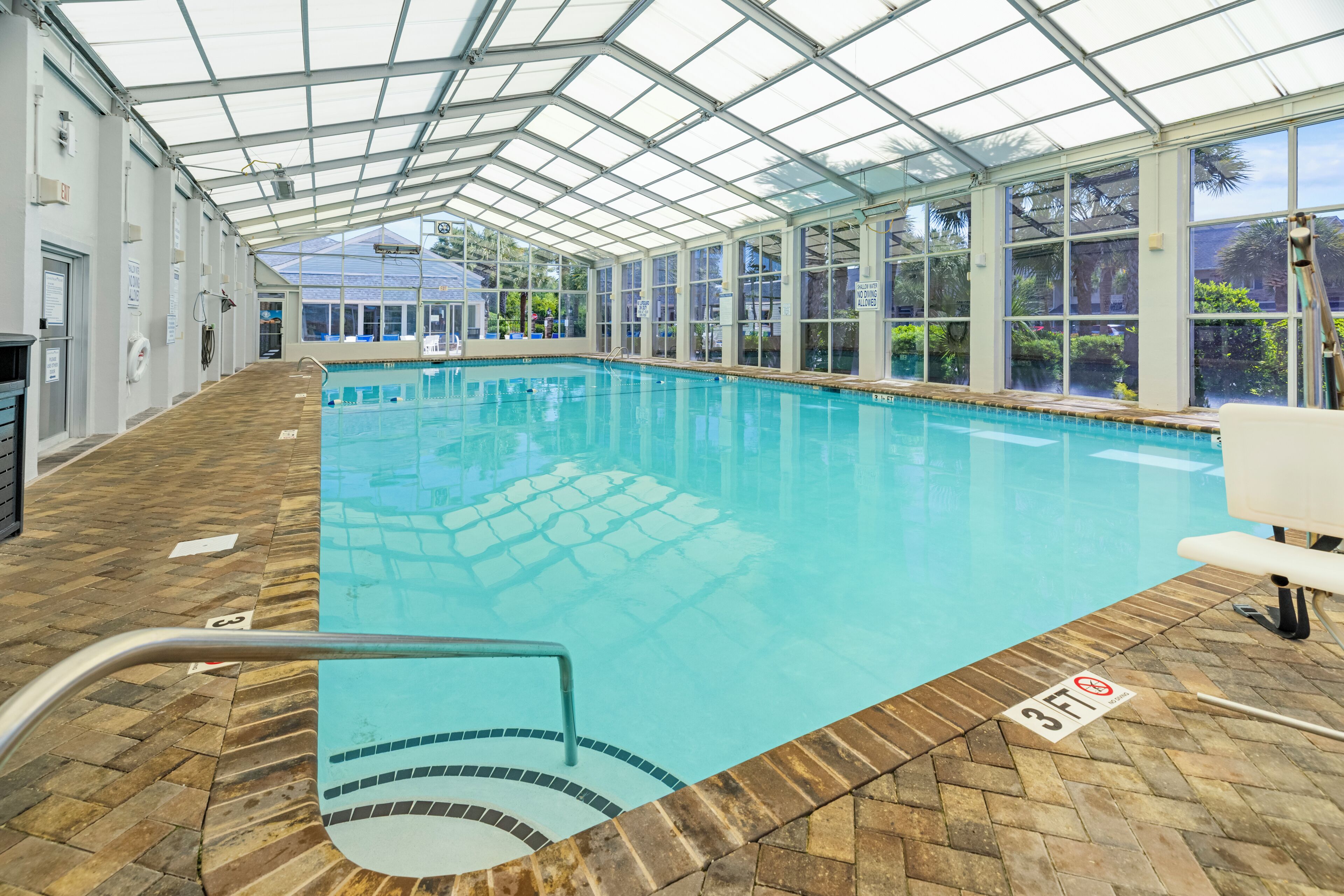 Indendørs swimmingpool med glasloft, klart område ved poolen og et skilt, der angiver 3 fod dybde - må ikke dykke.