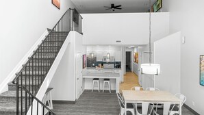Un interior moderno con una escalera, un comedor con mesa y sillas, y una cocina al fondo.