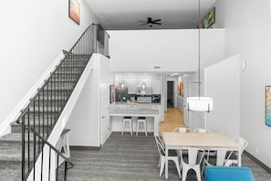 A modern interior with a staircase, a dining area with a table and chairs, and a kitchen in the background.