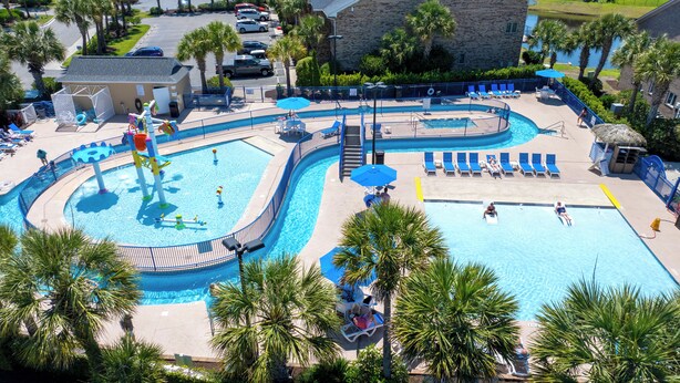 Una gran piscina al aire libre con varias pistas, tumbonas y un tobogán de agua.