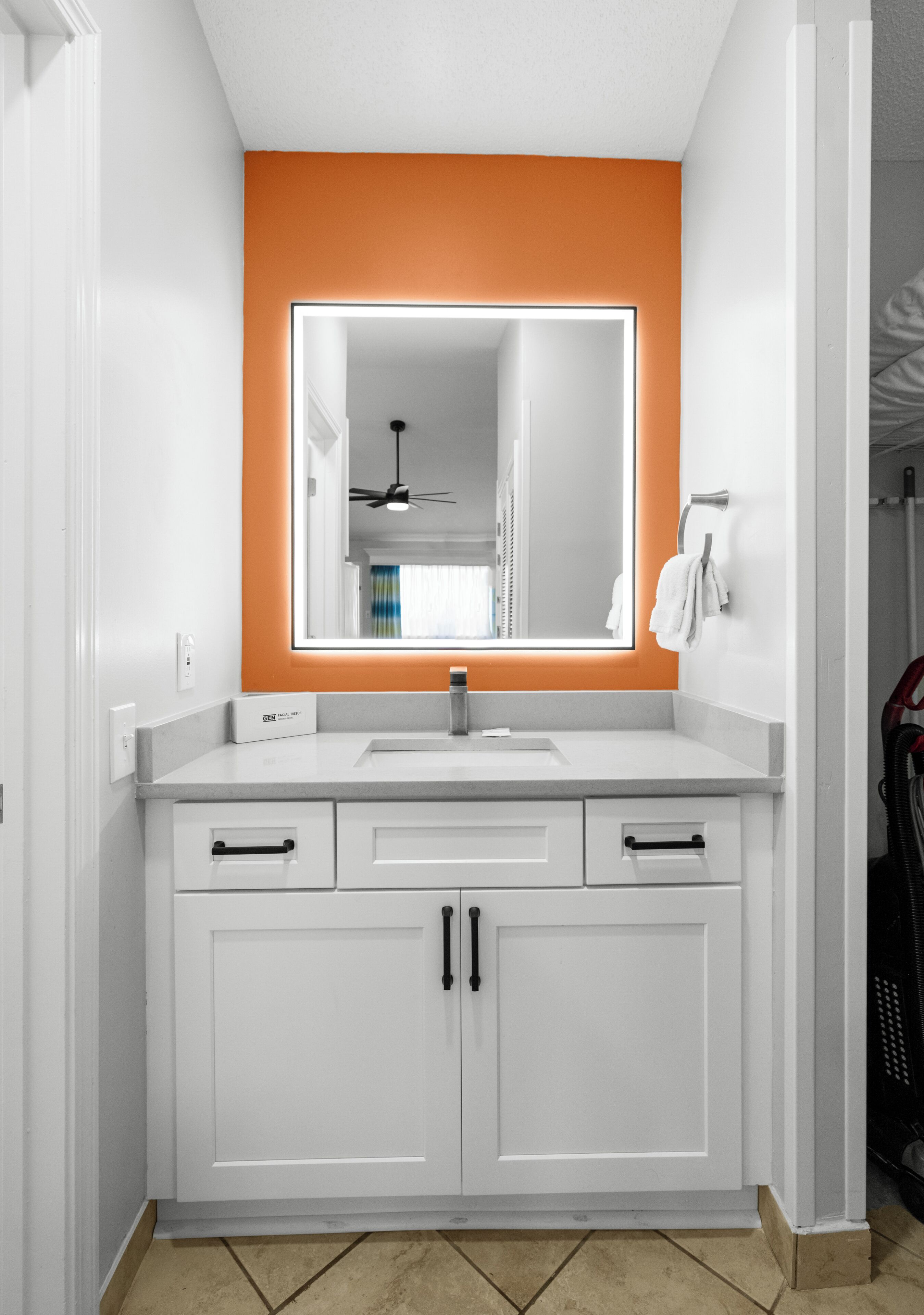 Een badkamer met een witte wastafel, een spiegel met oranje rand, een plafondventilator en een handdoekrek.