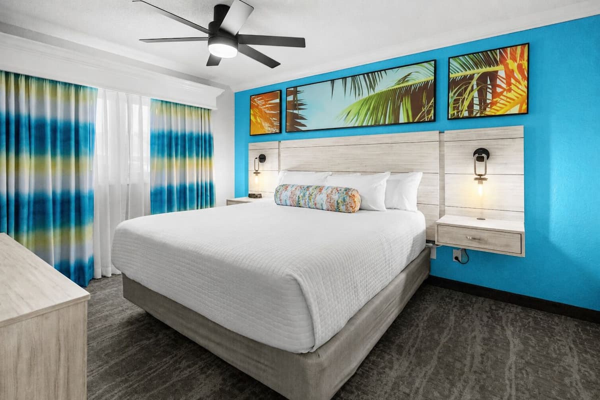 A hotel room with a large bed, a ceiling fan, a nightstand with a lamp, and a wall with three framed pictures.