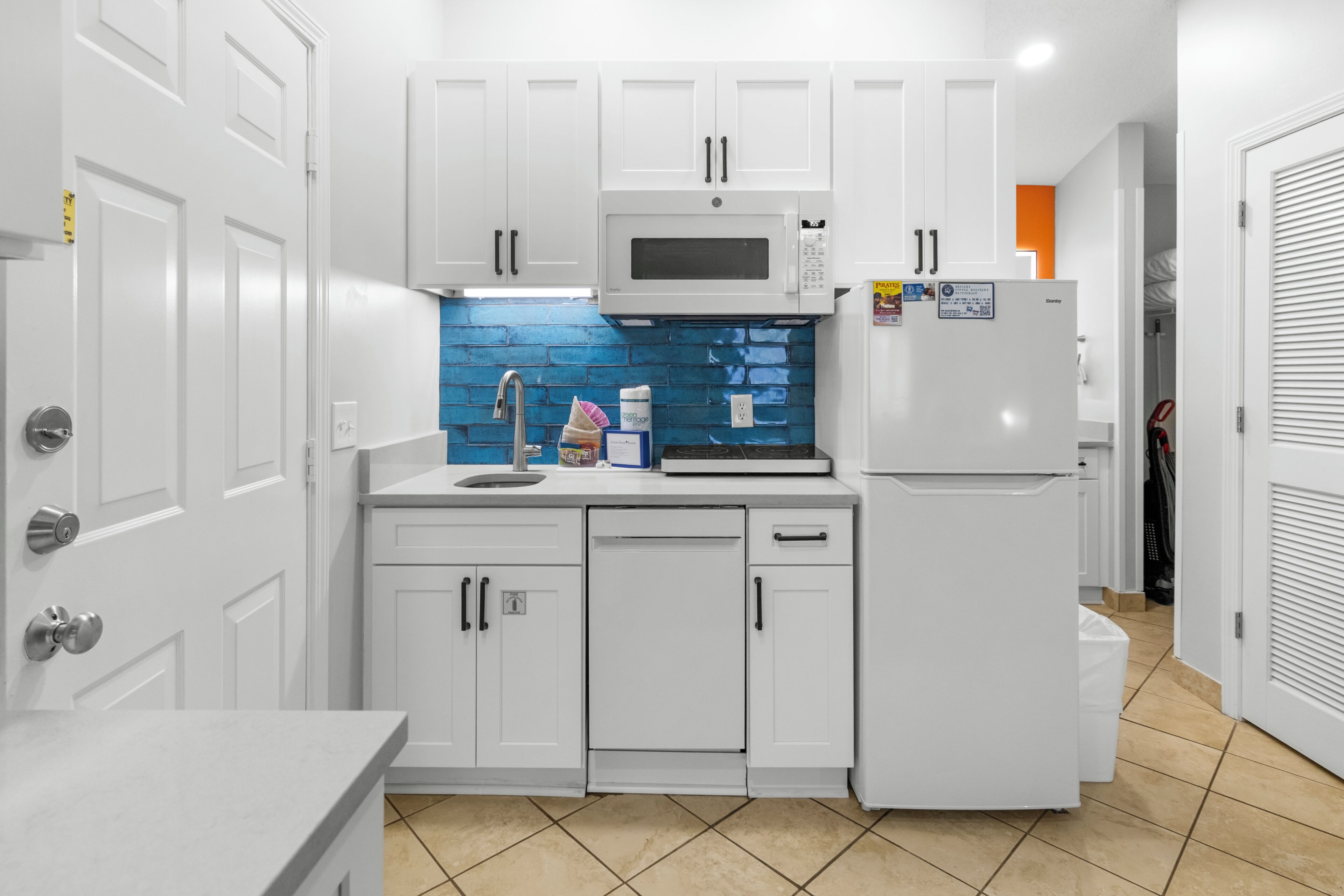 A compact kitchen with white cabinetry, a microwave, a refrigerator, and a blue-tiled backsplash.