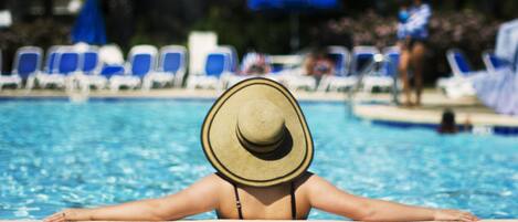 En person slapper af ved en pool med liggestole og parasoller i baggrunden.
