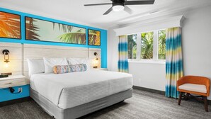 Un dormitorio con cama, mesitas de noche, ventilador de techo, ventana con cortinas y una silla.